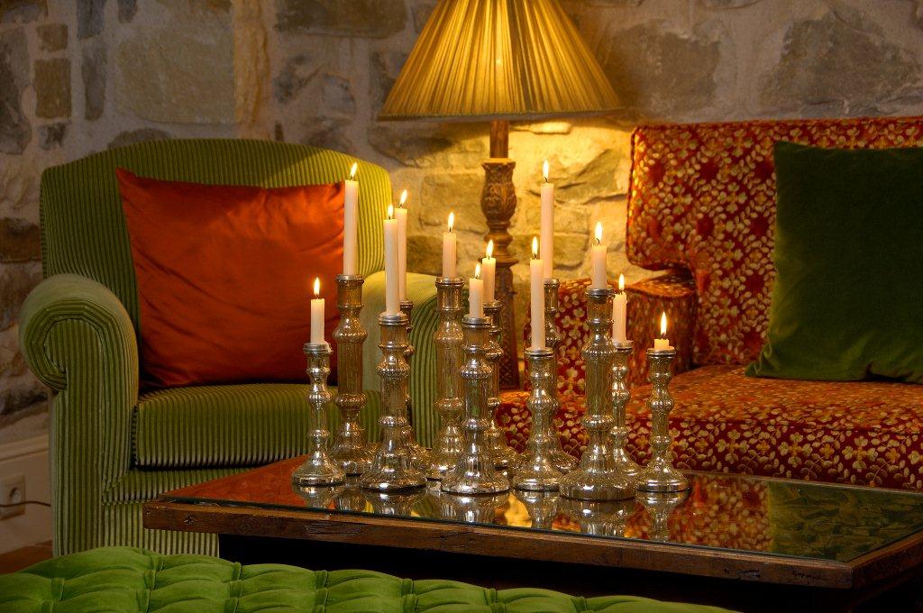 Candlelit lounge with silver candlesticks, green velvet chair, stone walls